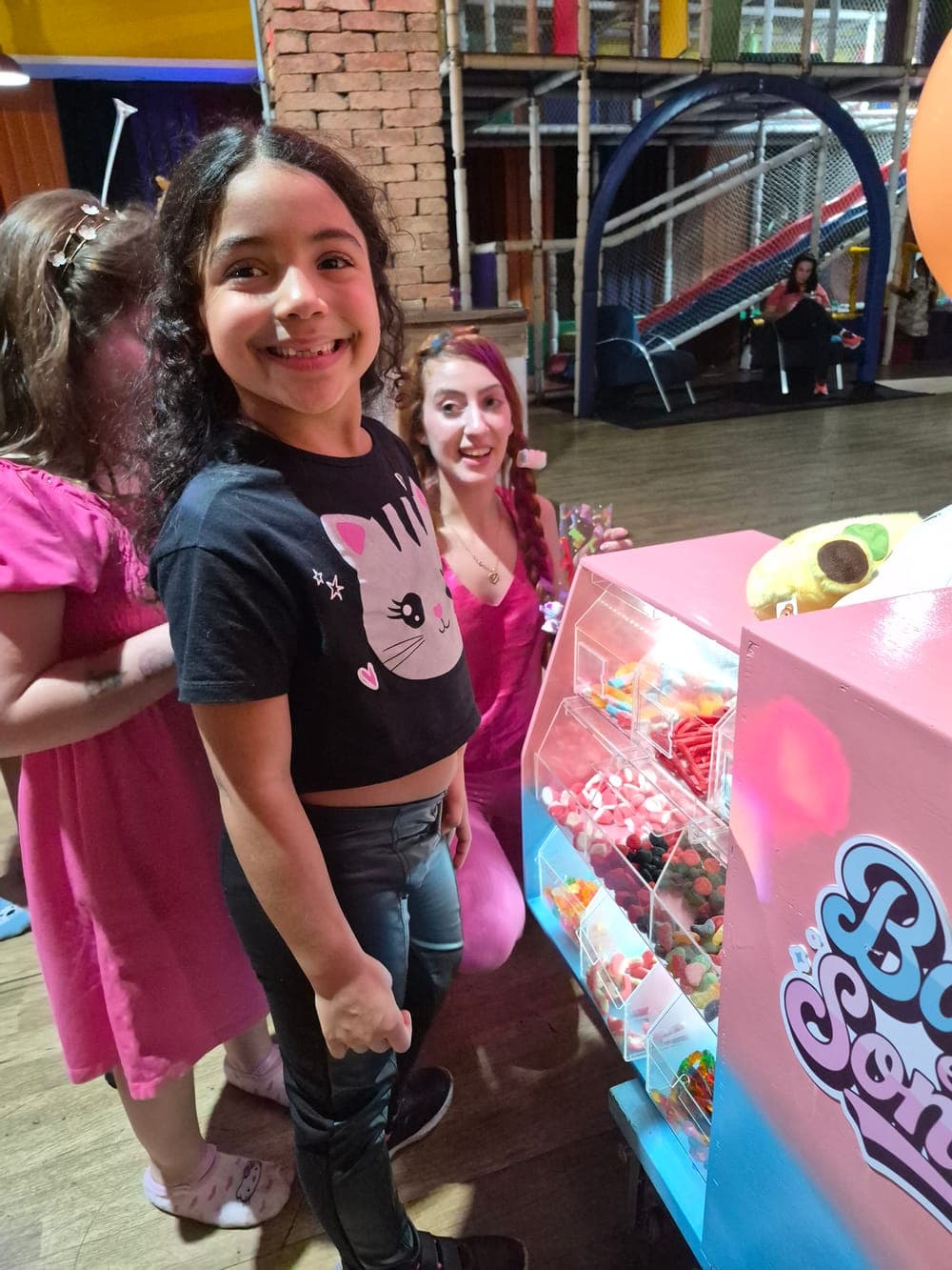 Menina sorrindo ao lado do carrinho, com uma integrante da equipe sorrindo ao fundo