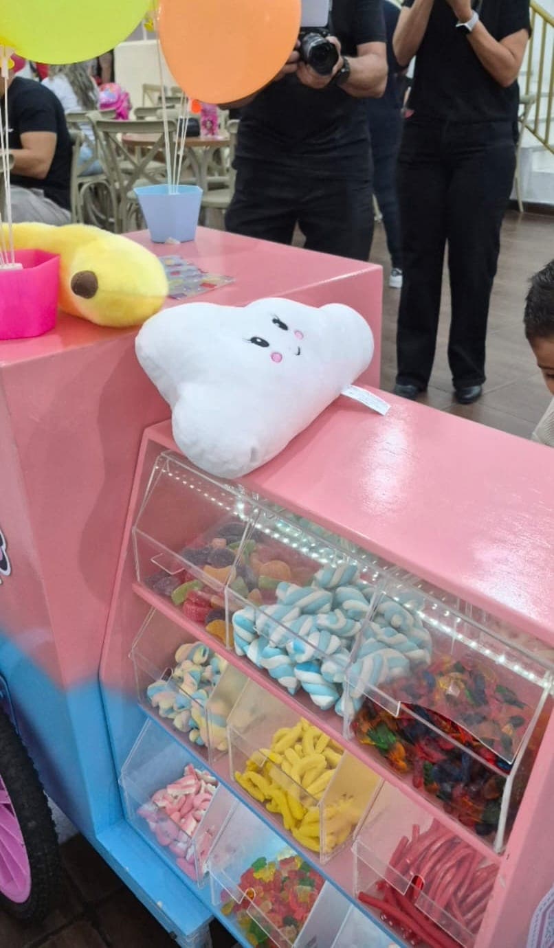 Vista de perto do carrinho rosa com potes de acrílico iluminados: marshmallows, bananinhas, minhocas e tubos azedinhos
